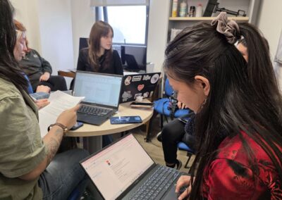 Una estudiante periodismo, vestida de rojo, tiene su computador portátil en las piernas mientras revisa la planificación del proyecto de diseño gráfico.